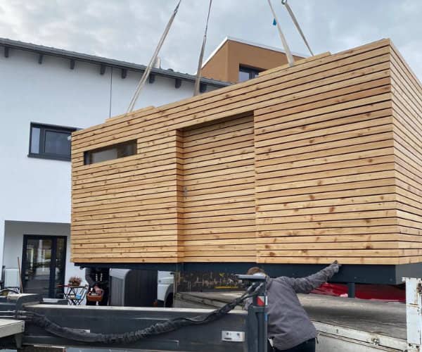 Individueller Holzbau der Zimmerei Brandt eines maßgefertigten Fahrradschuppens aus Holz, der gerade mit einem Kran abgeladen und montiert wird.