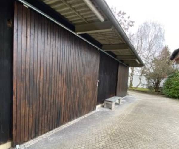 Seitenansicht eines individuell hergestellten Holztors mit Überdachung. Maßgefertigtes robustes Scheunentor aus dunklem Holz von unserer Zimmerei.