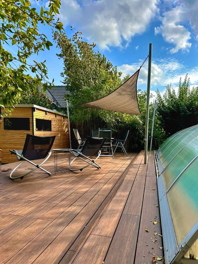 Moderne Holzterrasse mit Sonnensegel und stilvollen Gartenmöbeln bei schönem Sommerwetter, unser individueller Holz- und Terrassenbau in Braunschweig und Umgebung.