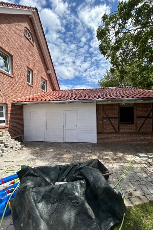 Außenansicht eines neu gebauten Carports aus Holz mit Ziegeldach, passgenau an ein Wohnhaus angebunden