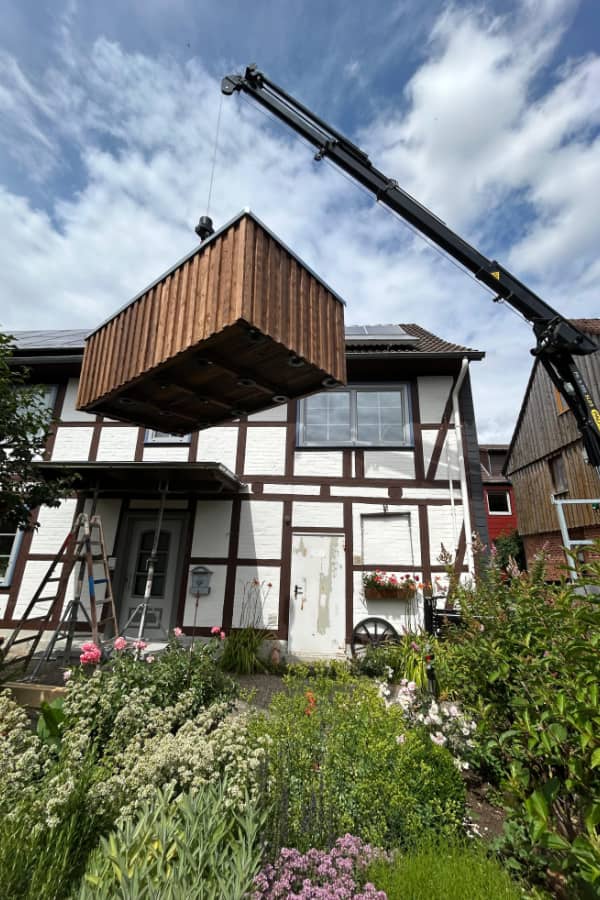 Kran hebt einen vorgefertigten Balkon aus Holz zur schnellen Montage an der Hausfassade