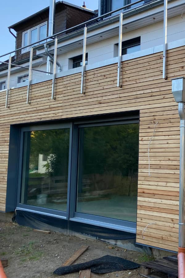 Zeitgemäße Rhombus-Holzfassade mit bodentiefen Fenstern und Balkonanschluss an einem Wohnhaus