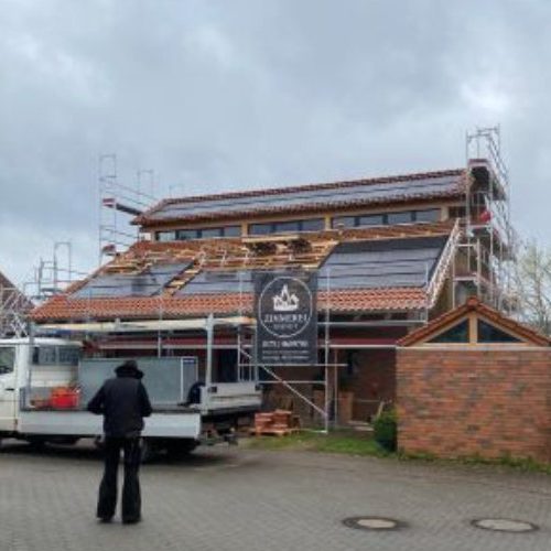 Zimmerer steht vor einem Dach, bei dem eine Solaranlage installiert wird.
